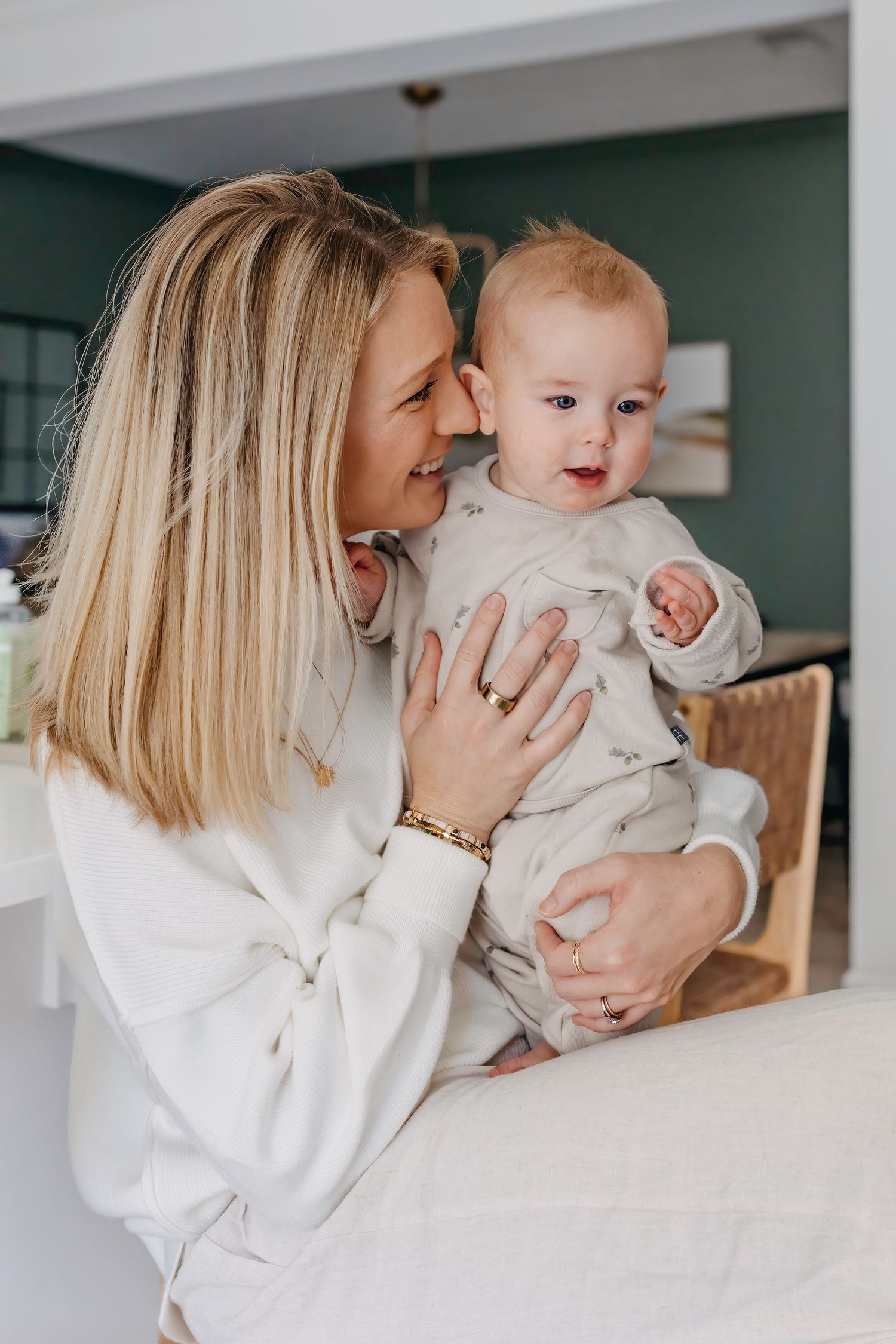 A tender moment between parent and baby wearing matching white outfits while sharing smiles in a home setting.