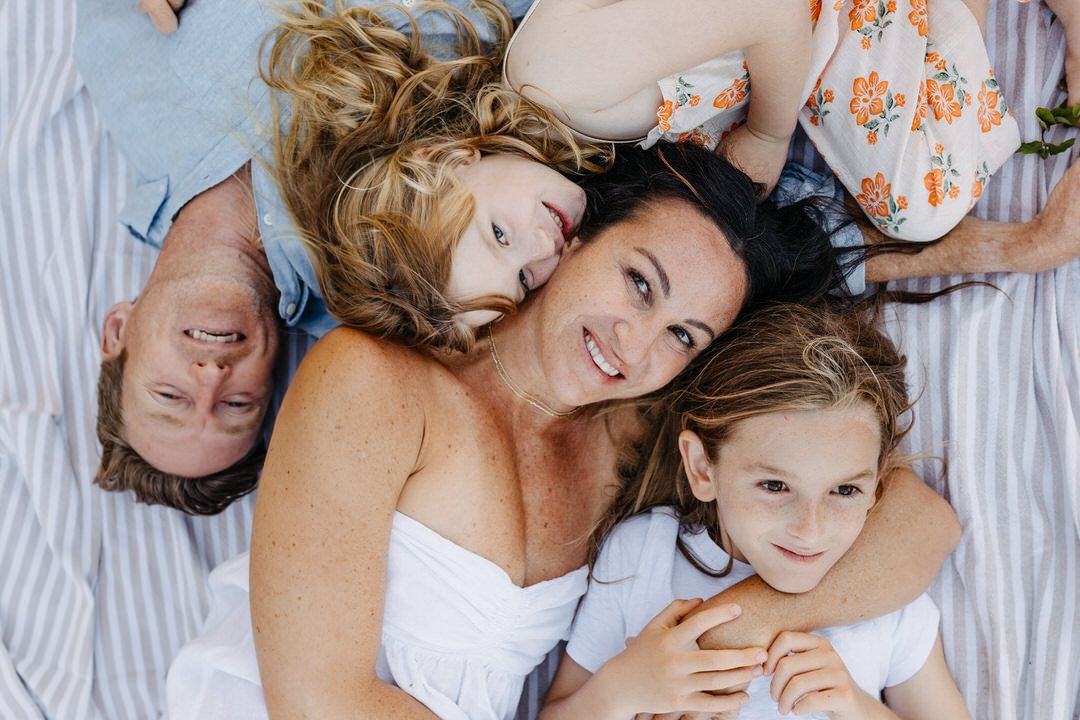 A family of four lying on a blanket while laughing and having fun together.