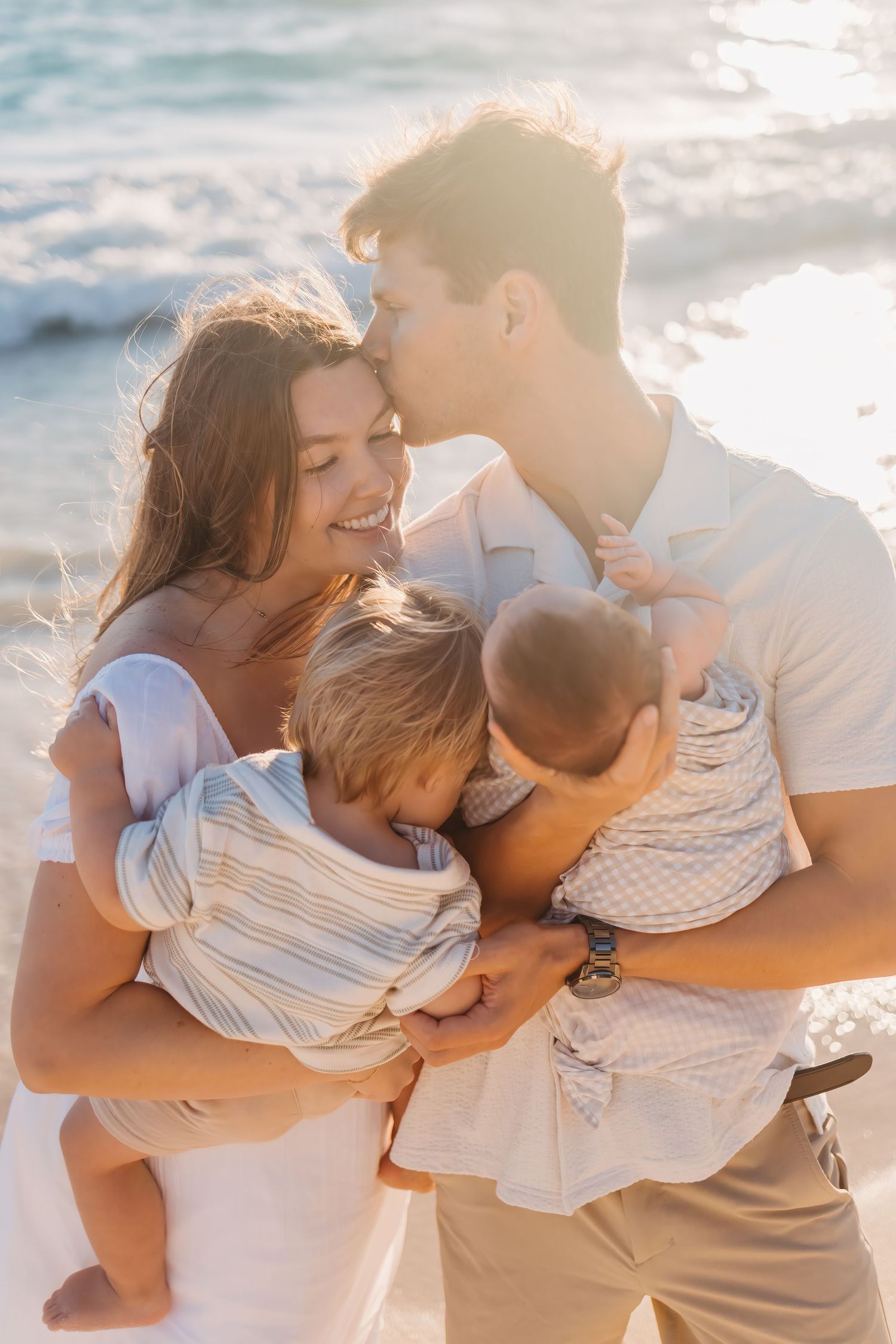 A loving family shares a tender moment together on the beach at sunset with warm golden light surrounding them.