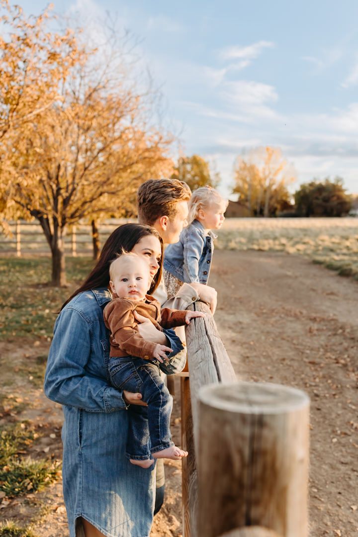 Family enjoying an autumn day outdoors with fall foliage and wooden posts in a rustic setting.