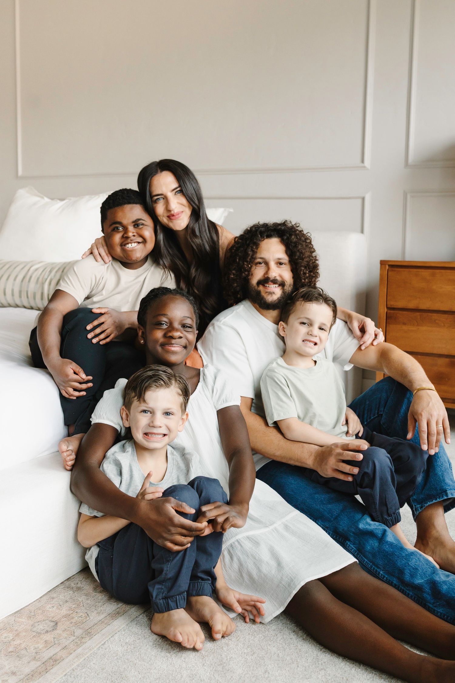 A happy family lounges together on a bed, sharing joyful moments in casual denim and white outfits.
