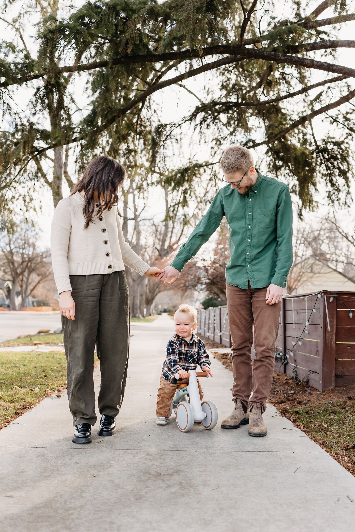 parents holding hands with toddler on bike in between them