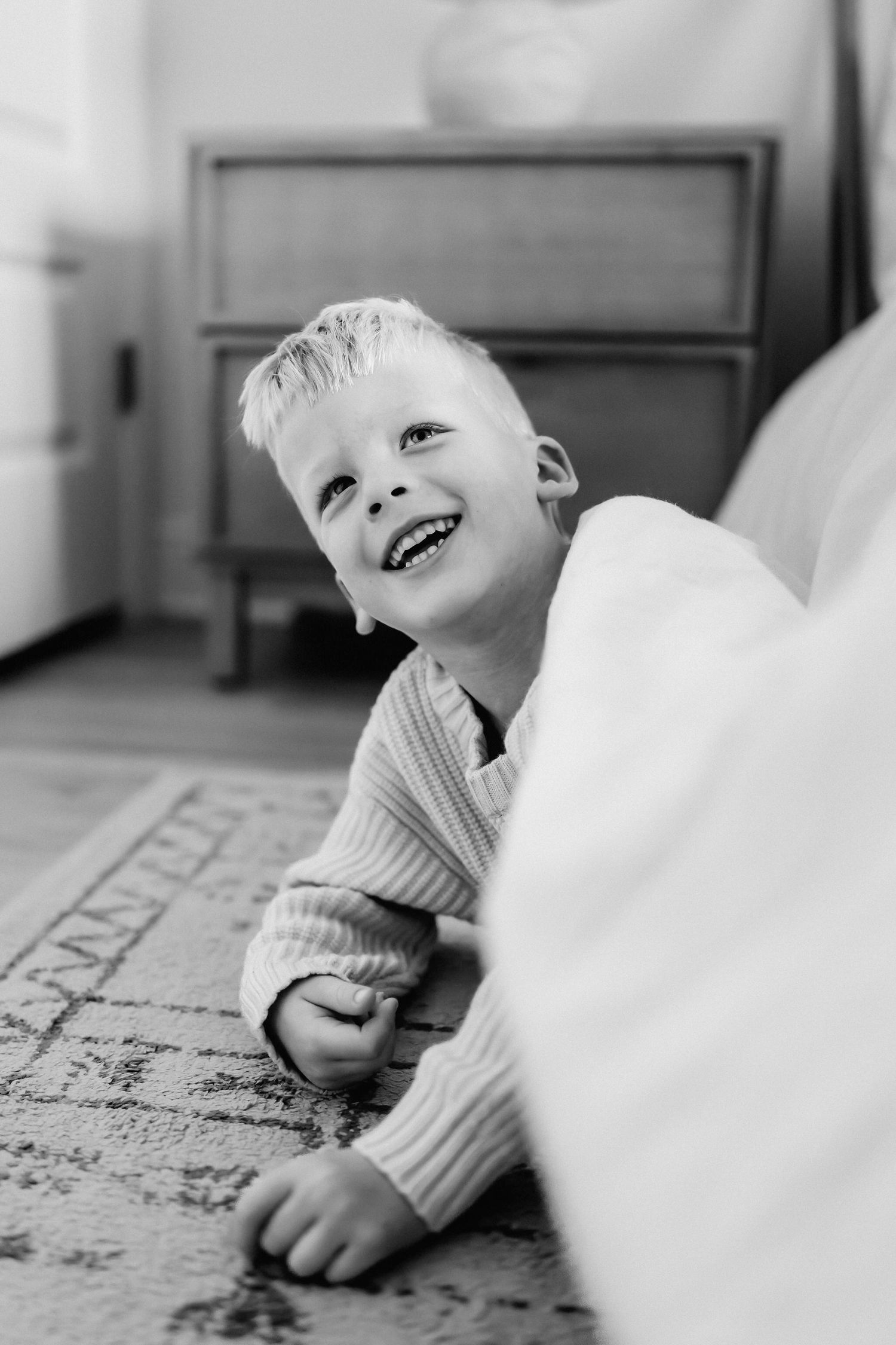 A young child lies on a patterned rug while laughing joyfully in black and white photography.