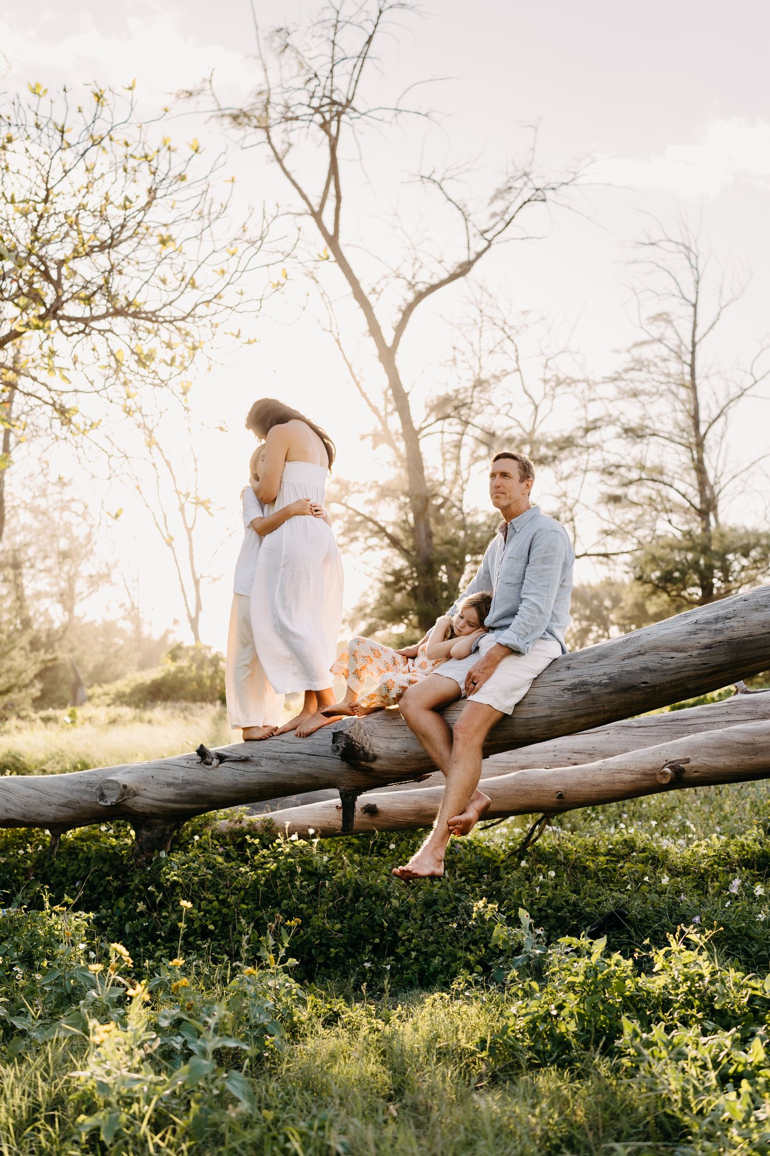 family sitting together on fallen log at sunset in field of yellow wildflowers during outdoor photo session.