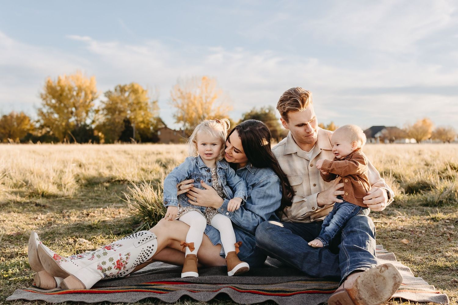 A family sits together on a blanket in a golden autumn field during sunset.