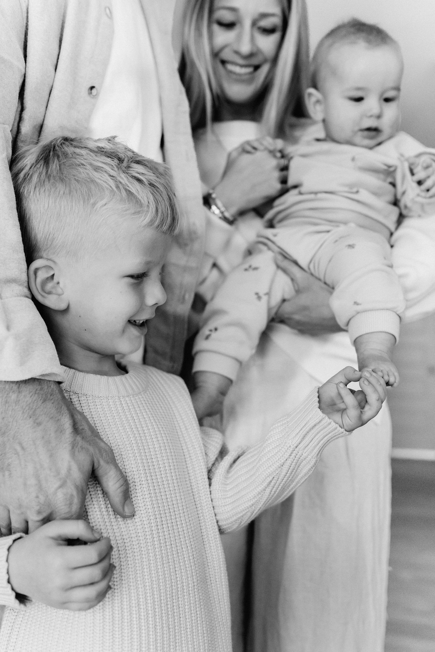 Black and white candid photo series showing tender moments between parents and babies in matching white outfits.