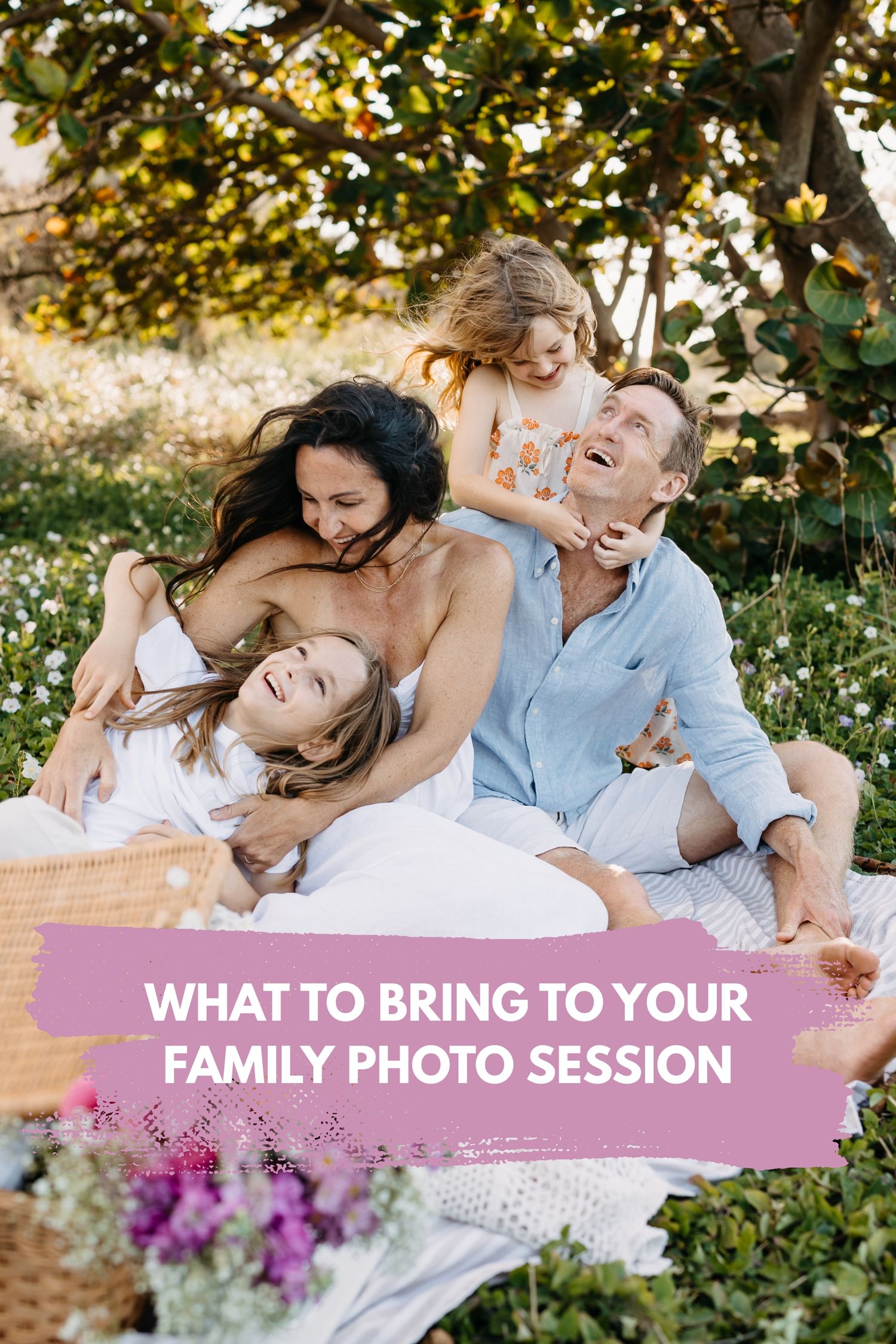 A family in coordinated white and blue outfits laughs together while laying on grass during an outdoor photo session.