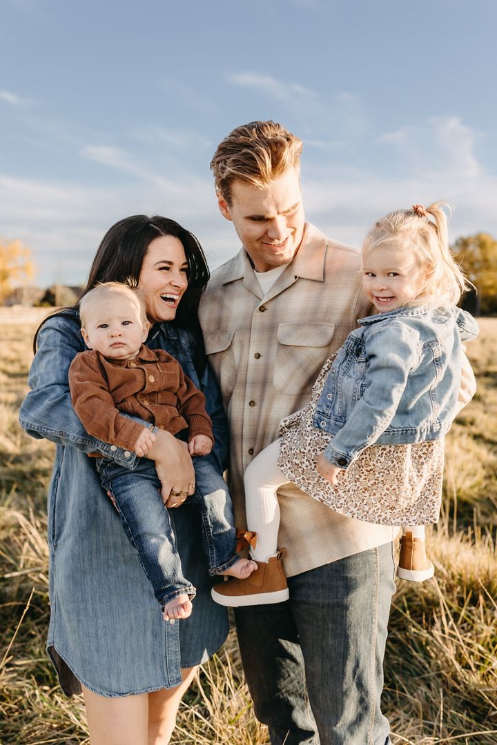 Family enjoying playful moments together in a golden field during sunset, creating joyful candid portraits.