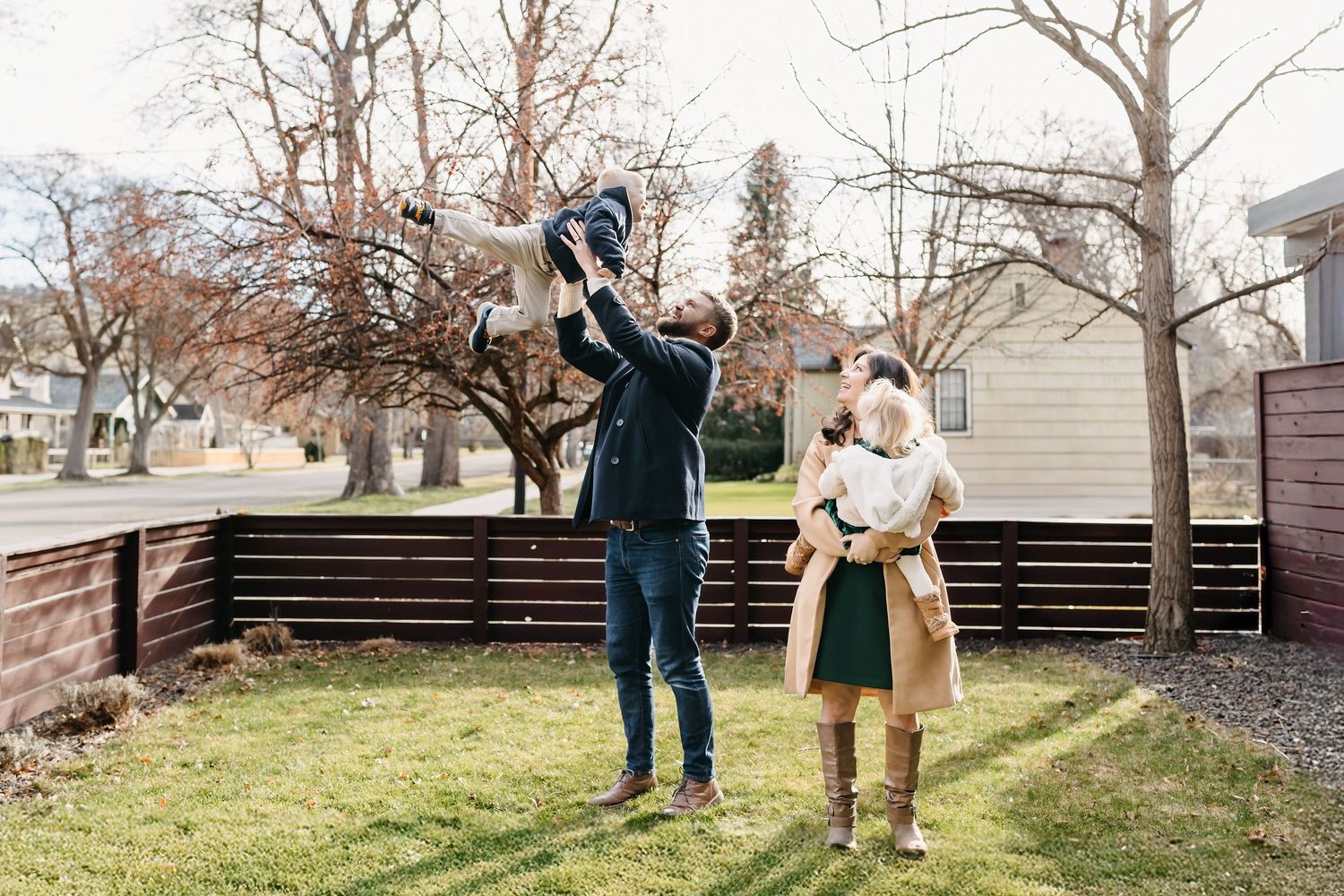 People playing together in a backyard with bare trees and wooden fence on an autumn day.