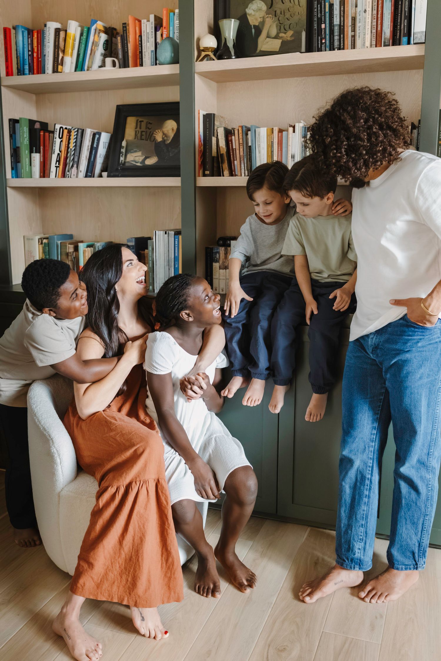 A joyful gathering of people sitting and laughing together by a bookshelf in a cozy office.