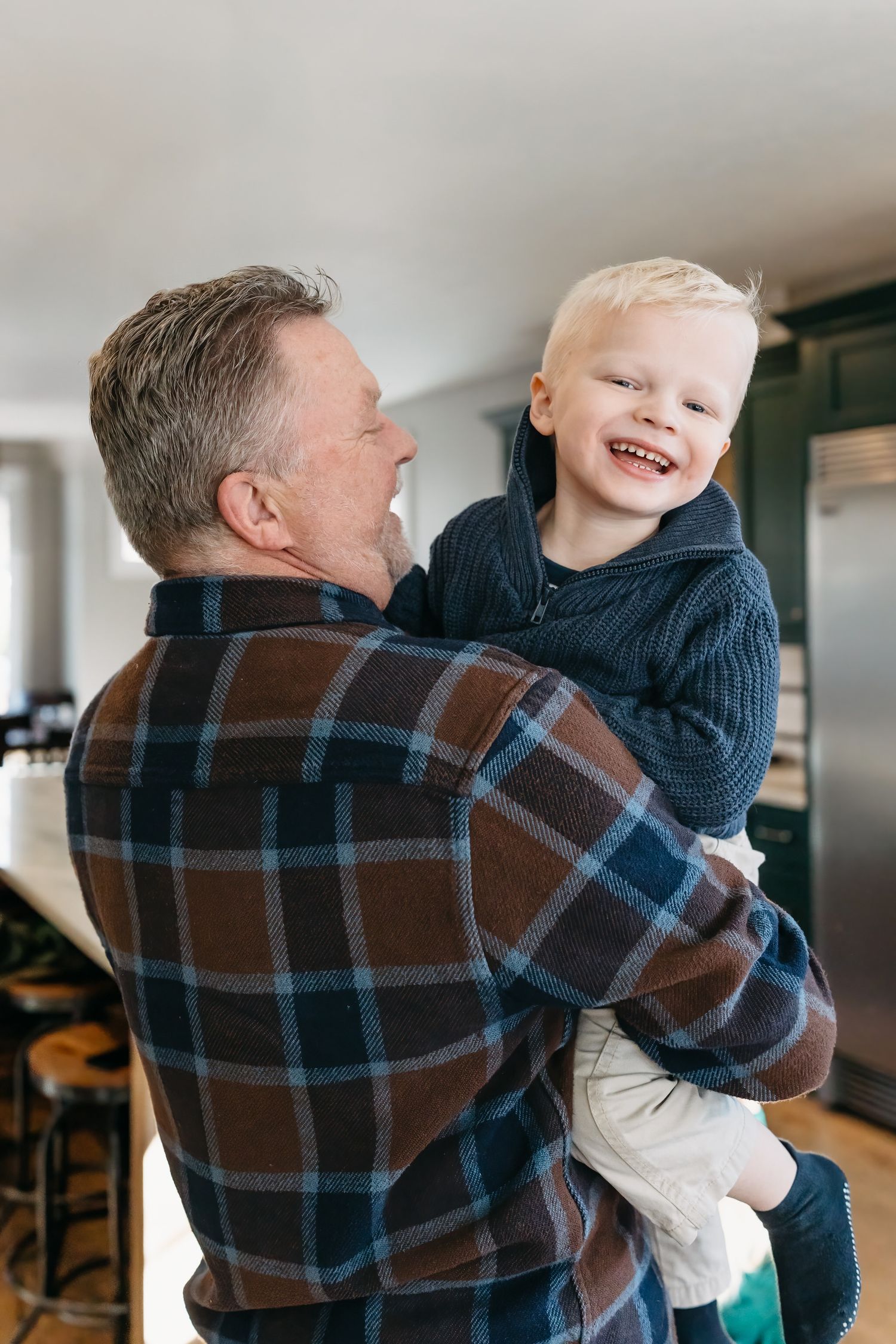 A heartwarming photo shows a playful interaction between grandfather and grandson in a plaid shirt and navy sweater sharing joyful moments.