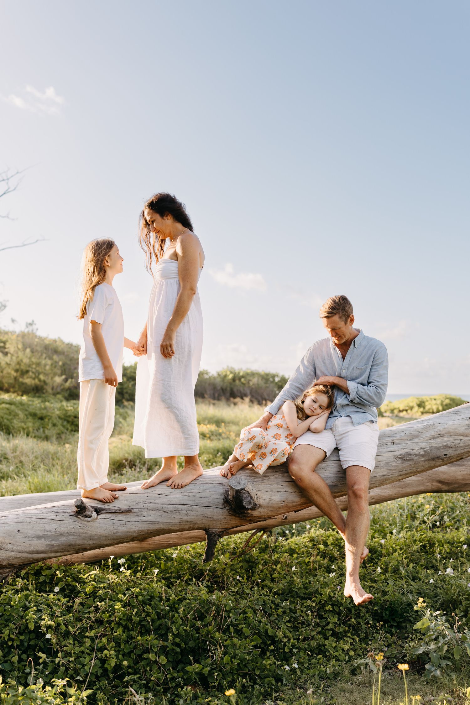 Family sitting together on a rustic wooden log in a sunny meadow during golden hour.