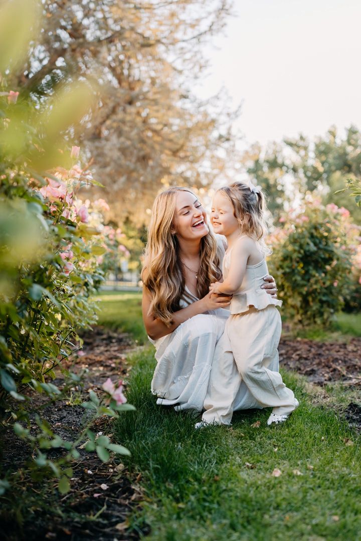 A tender moment shared between two figures in matching light blue dresses sitting in a blooming garden at sunset.
