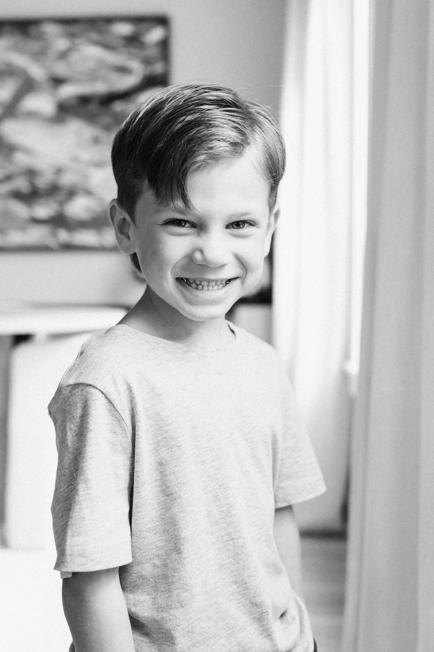 A young child wearing a gray t-shirt smiles brightly in a series of connected black and white portrait photos.