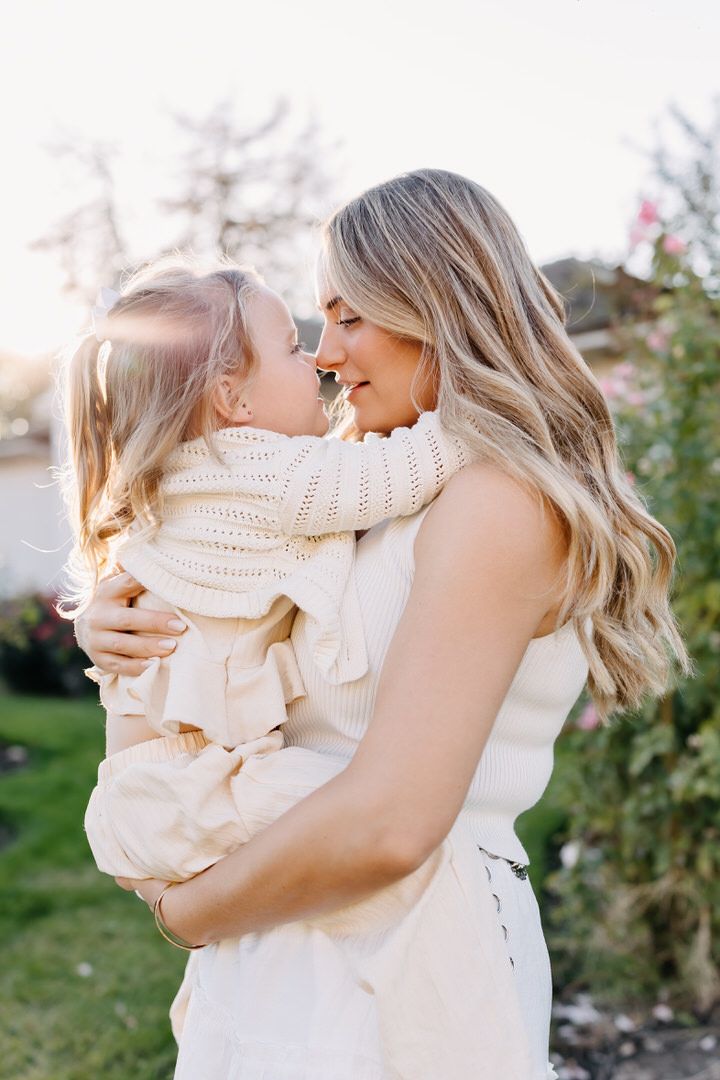 A tender moment between parent and child wearing cream colored sweaters in an outdoor garden setting.