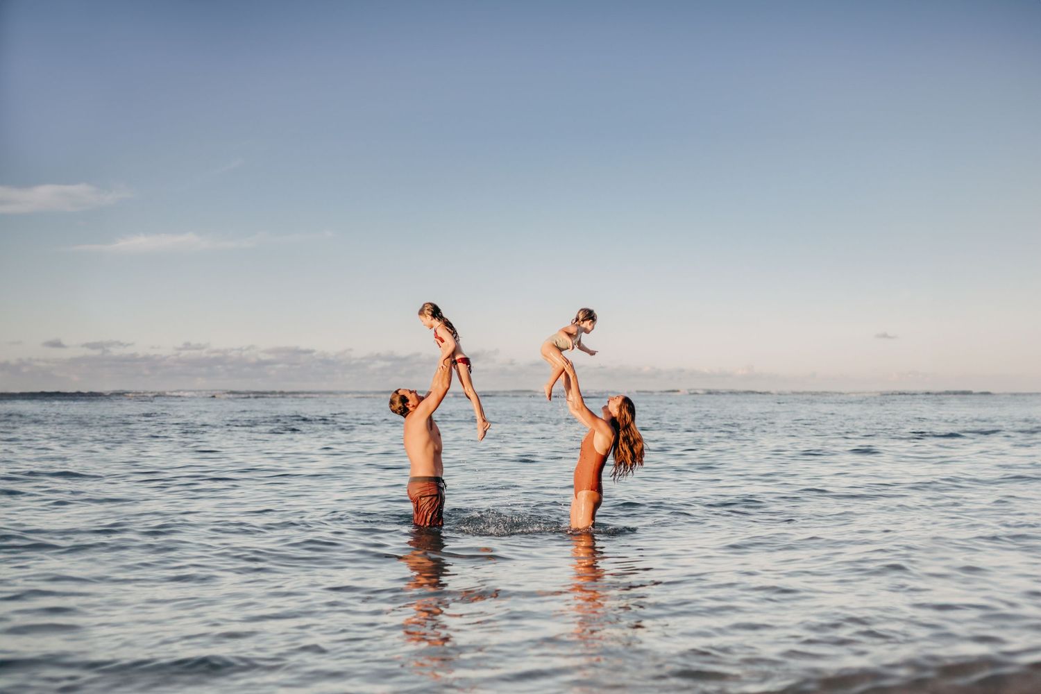parents playing with their daughters in the water during sunset
