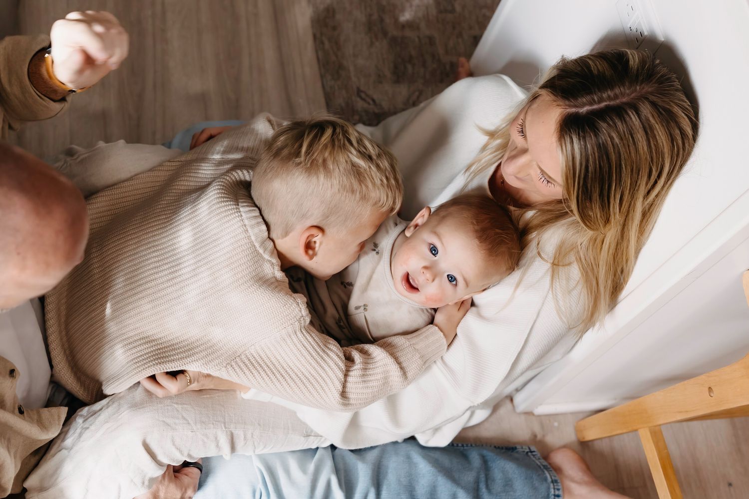 A cozy family moment captured on a white bed with warm knit blankets and soft natural lighting.