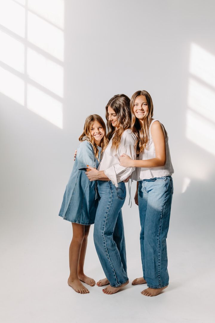 Group of people wearing denim and white clothing pose together against a white wall with dramatic shadows.
