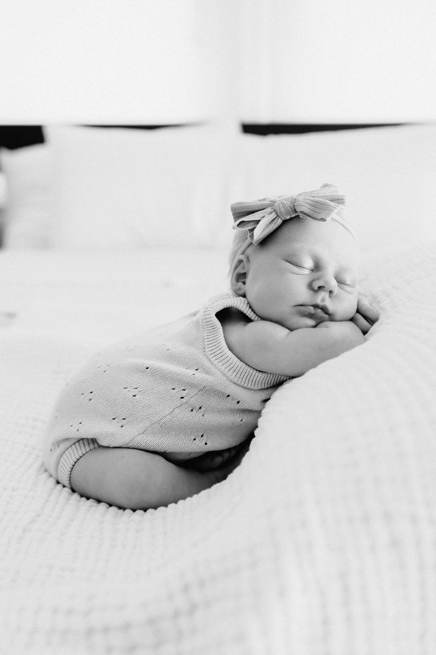 A sleeping newborn baby in white clothing rests peacefully on soft white bedding.