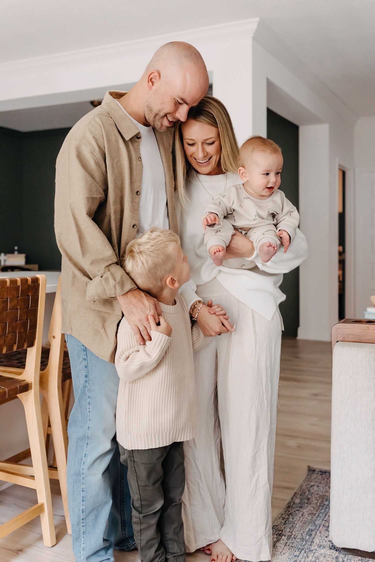 A family in neutral-toned clothing shares tender moments together in a bright modern home interior.