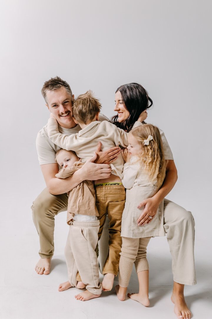 Family wearing neutral colored clothing share joyful moment together against white background in studio setting.