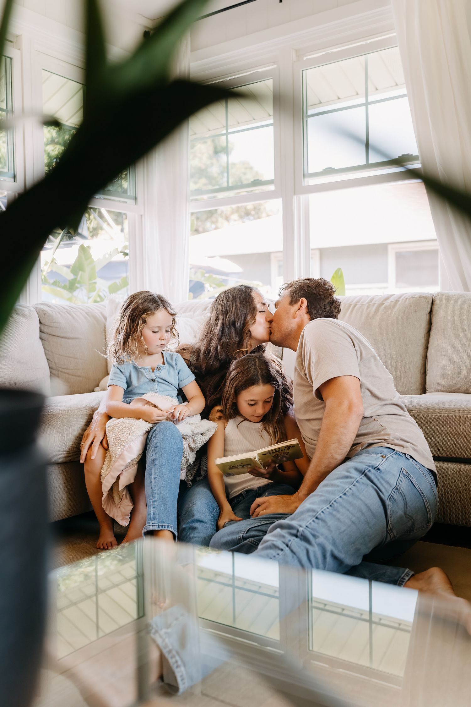 Family relaxing together on comfortable white couch in bright sunlit living room with window views.