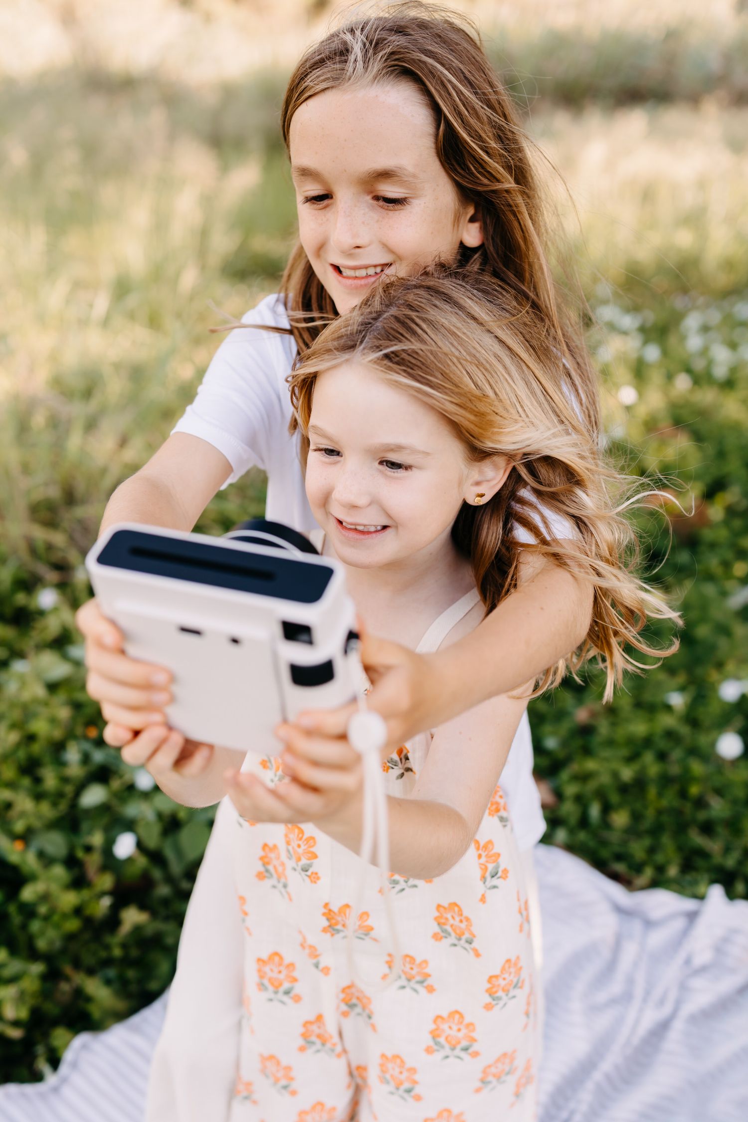 siblings enjoying a sunny outdoor moment while taking a selfie with a polaroid camera
