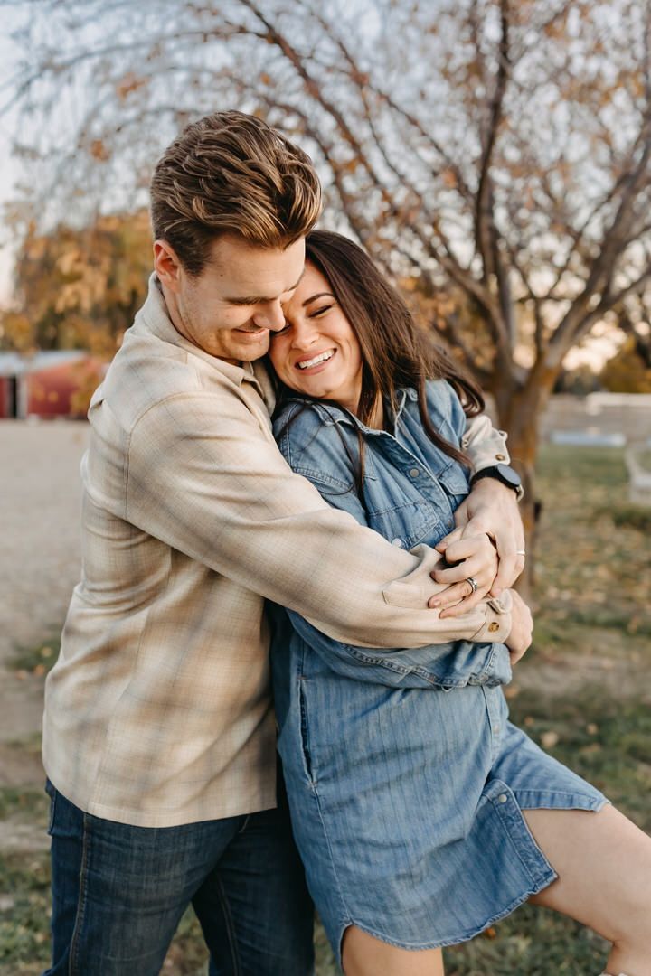 A couple shares intimate embraces and laughter in a casual outdoor autumn setting wearing denim and beige clothing.