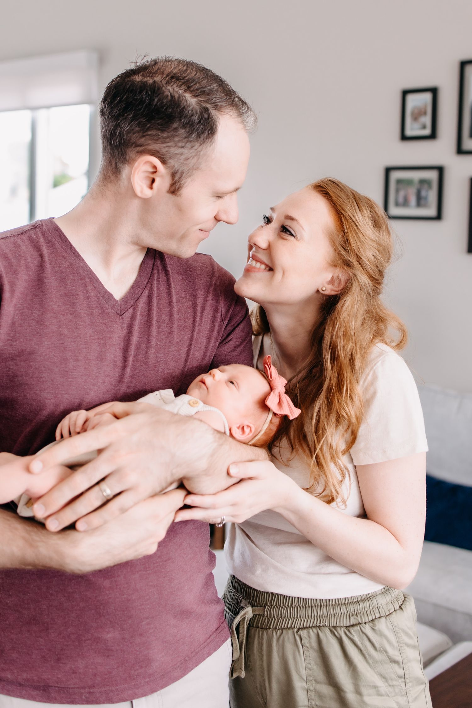 A couple shares tender moments while holding their newborn baby in a bright indoor setting.