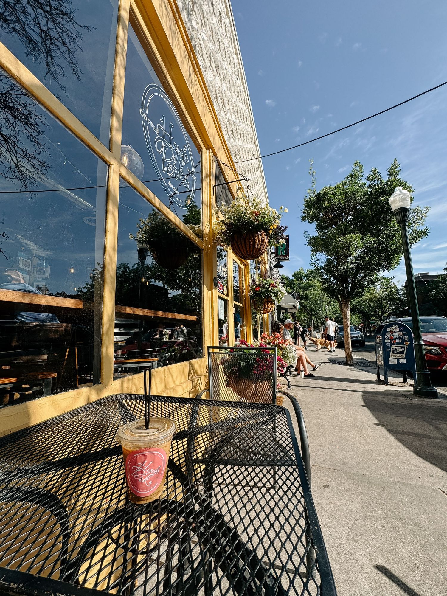 Panoramic view of a coffee shop in Hyde Park Boise with wooden beams and metal railings along a sunny sidewalk.