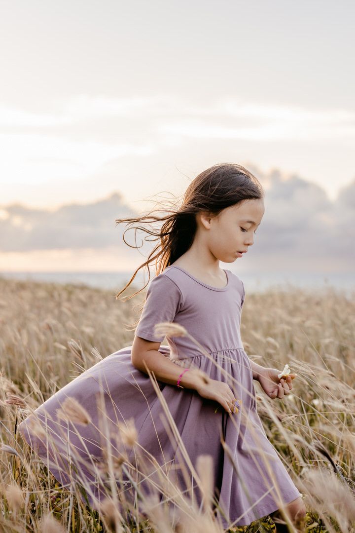 A child in a flowing purple dress runs joyfully through a golden wheat field at sunset.