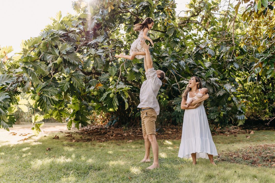 mom holds new baby while watching dad toss daughter in the air in an backyard photo session