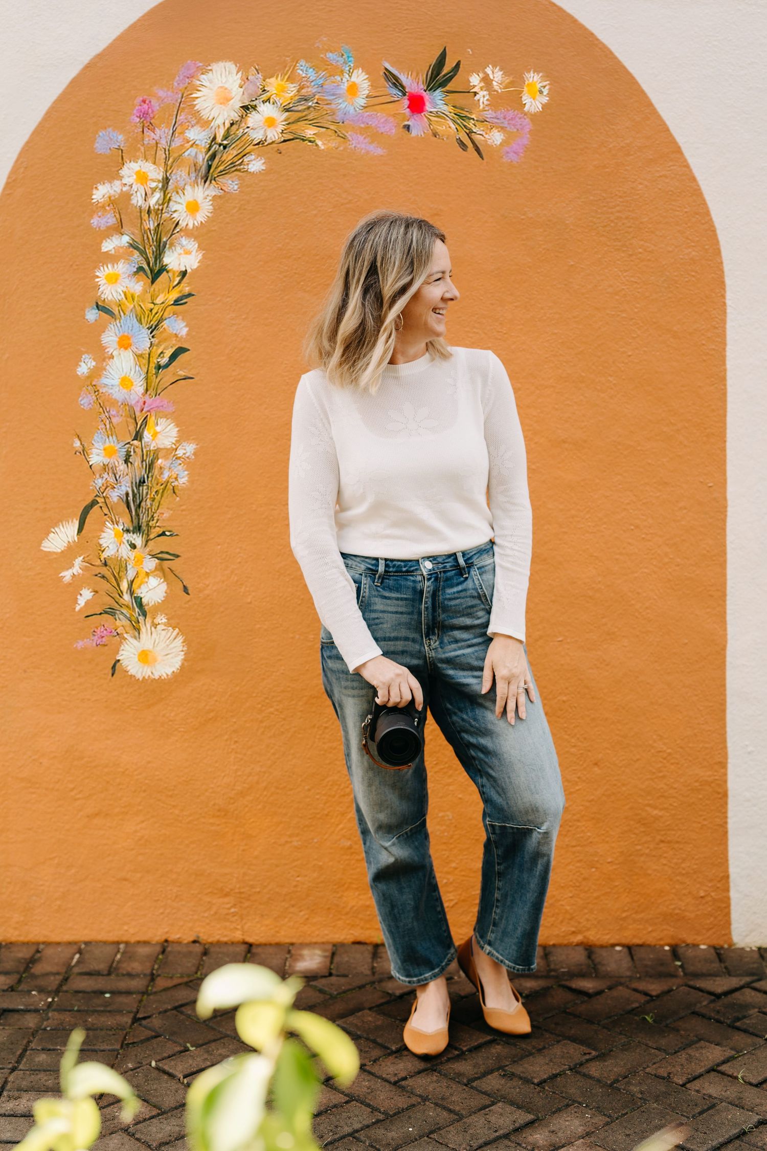 Person in white sweater and jeans poses against orange wall with floral decorations, showing different casual poses.