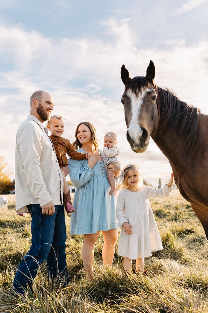 Family enjoying a tender moment together in a sunlit field with their beautiful horse at sunset.