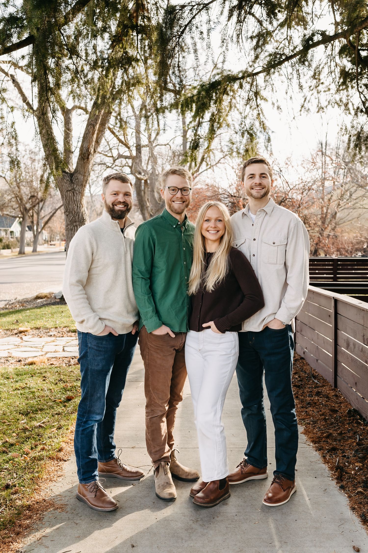 adult siblings standing under trees on the a sidewalk in boise for a family photo wearing earth tones