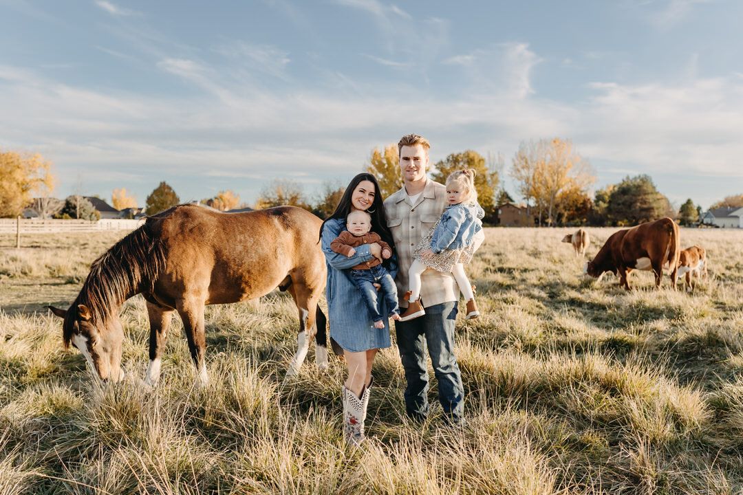a family dressed in denim, corduroy, and plaid in a pasture with a horse and cows during golden hour lighting.