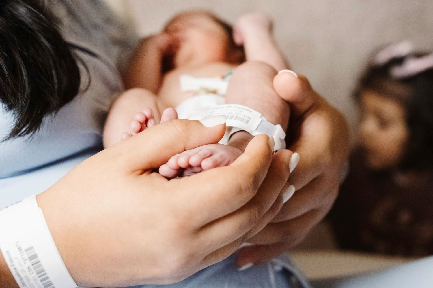 Close-up shot of hands tenderly holding a sleeping newborn baby wrapped in white blanket.