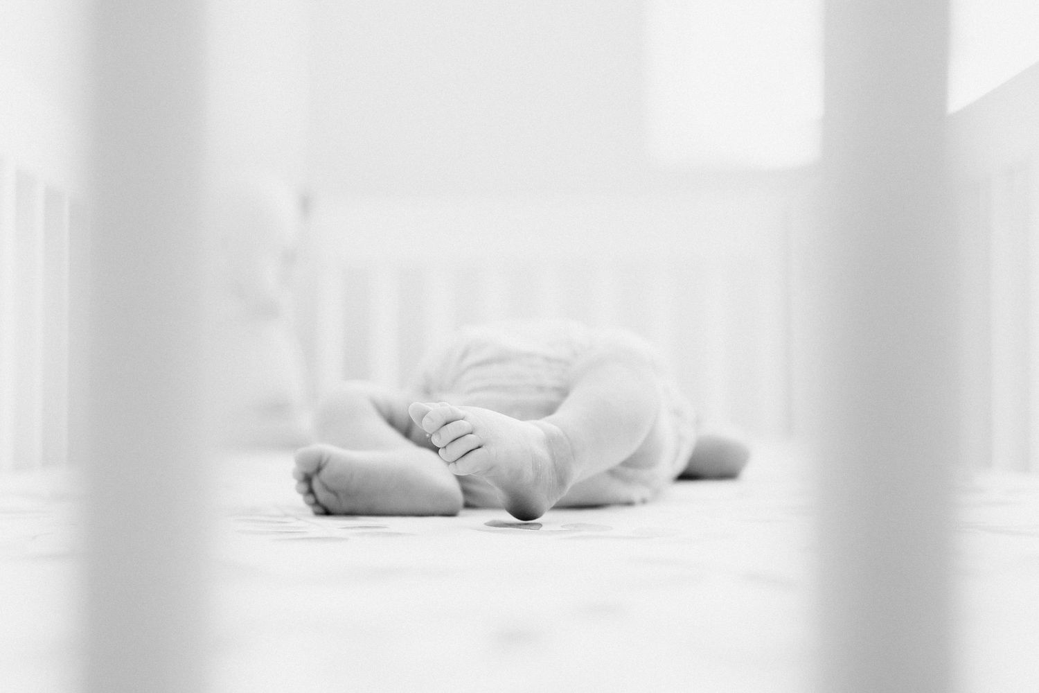 black and white image of newborns feet while laying in crib