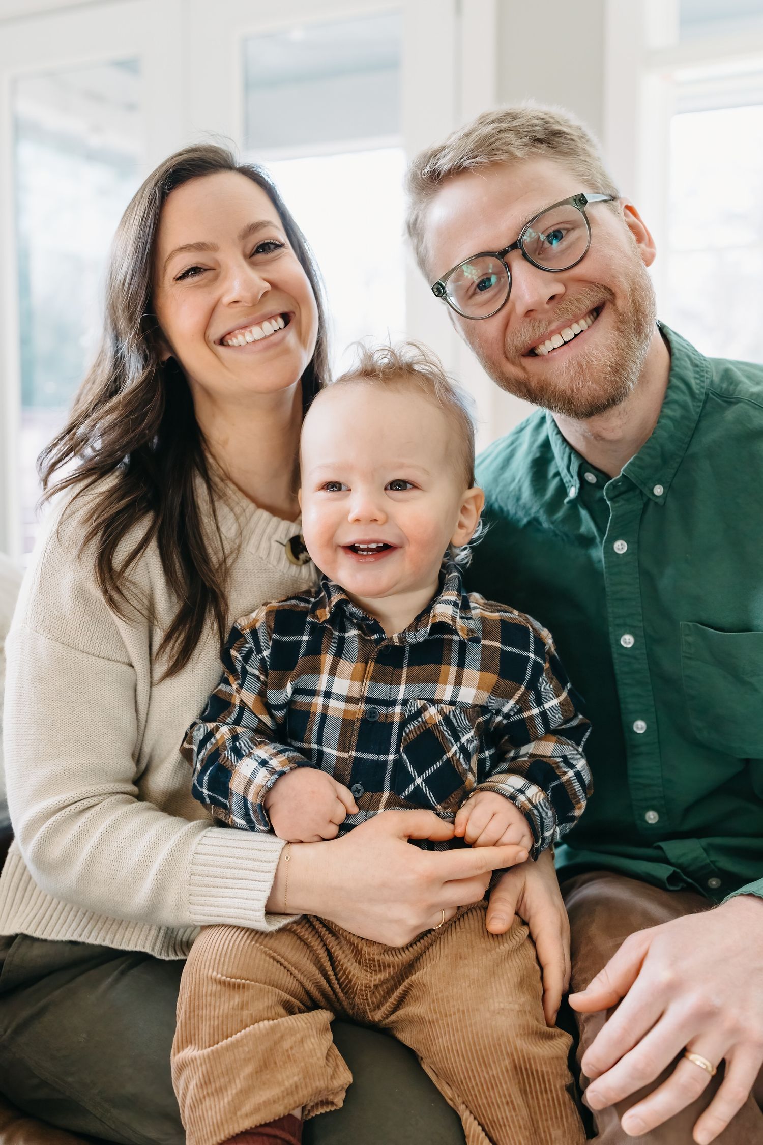 A family wearing green and neutral tones shares candid laughs and embraces while posing for casual portraits.