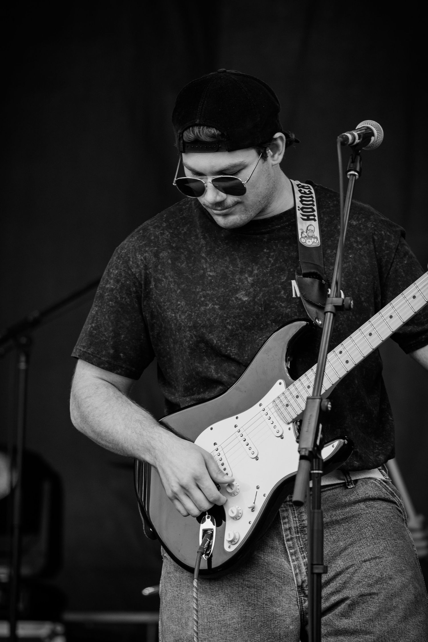 Close-up of guitarist playing white Fender Stratocaster on dark stage.