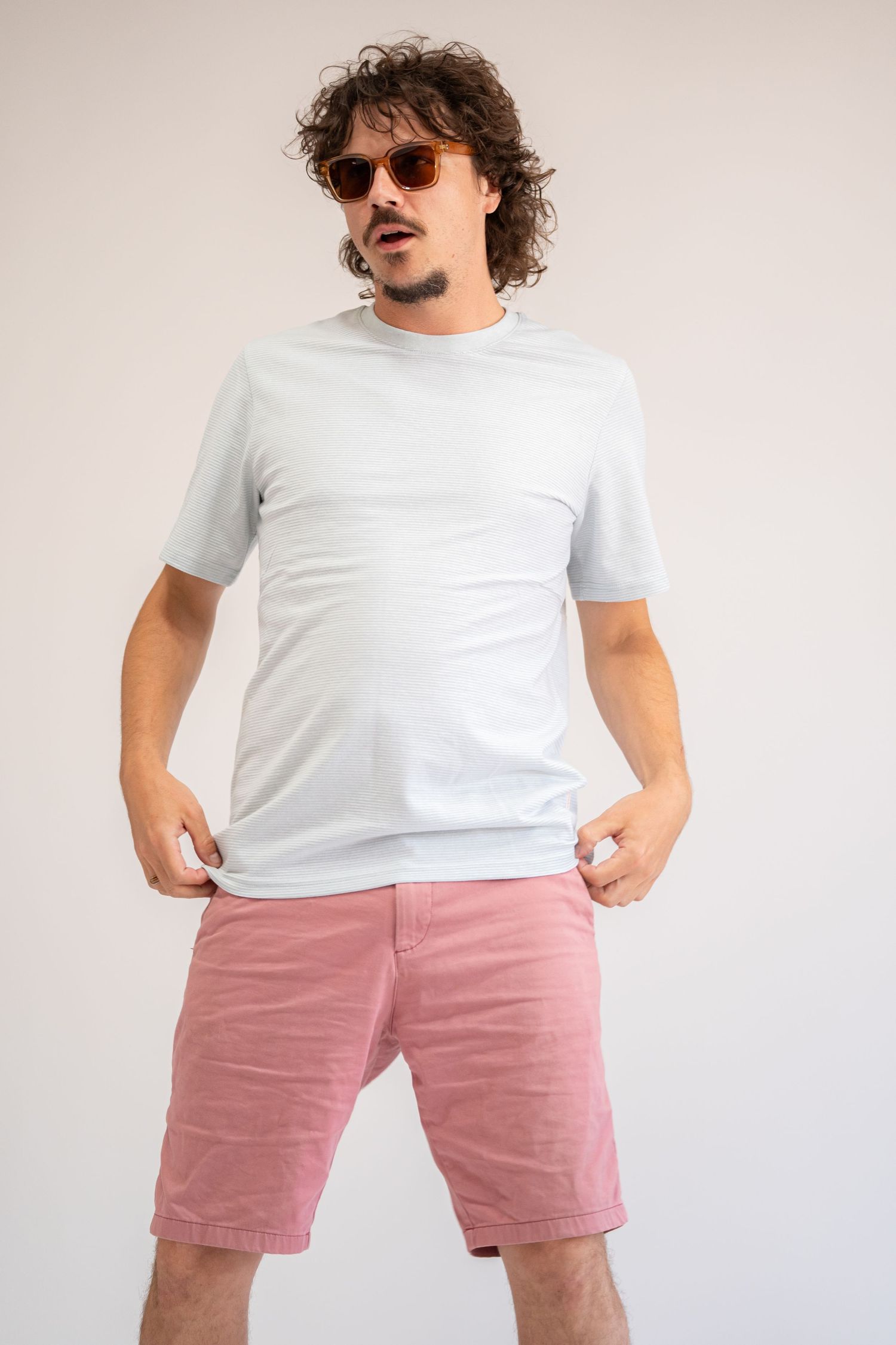 Person wearing white t-shirt and pink shorts in casual studio poses.