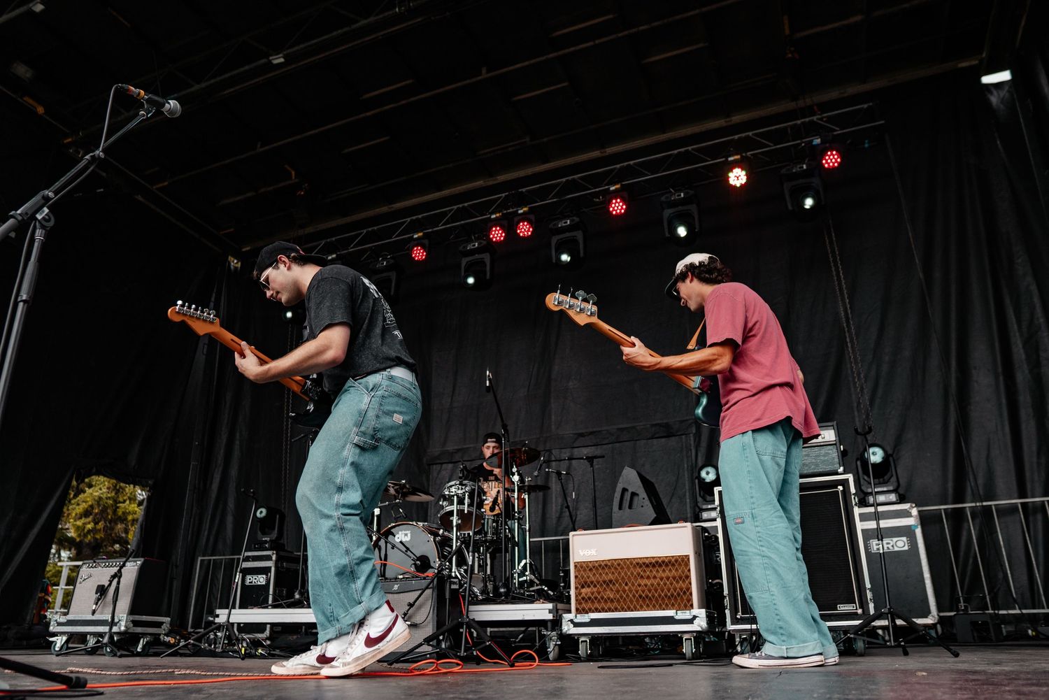 Wide shot of musicians performing on outdoor festival stage with dramatic lighting.