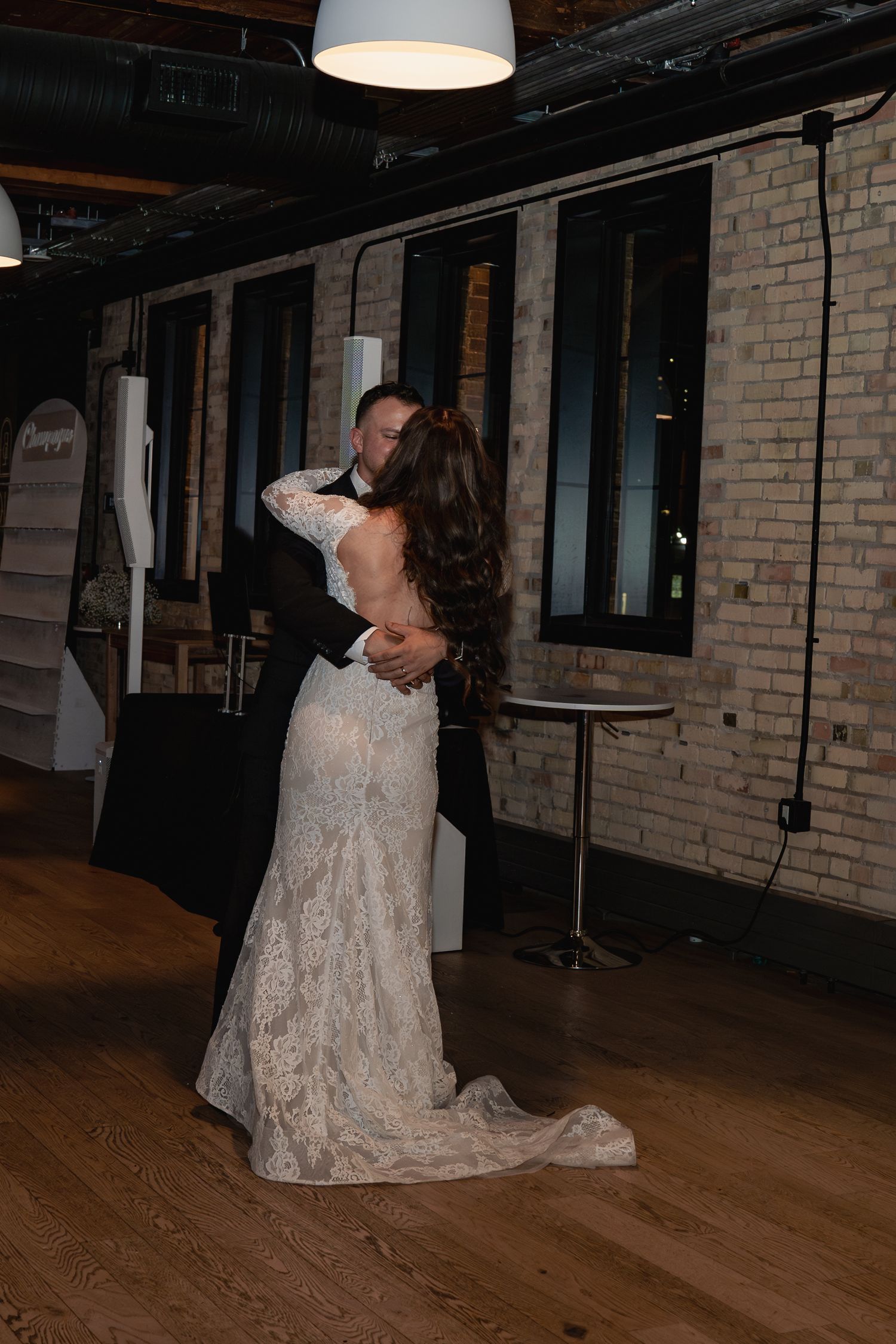 Couple dancing in industrial-style venue with exposed brick walls and wooden floors.