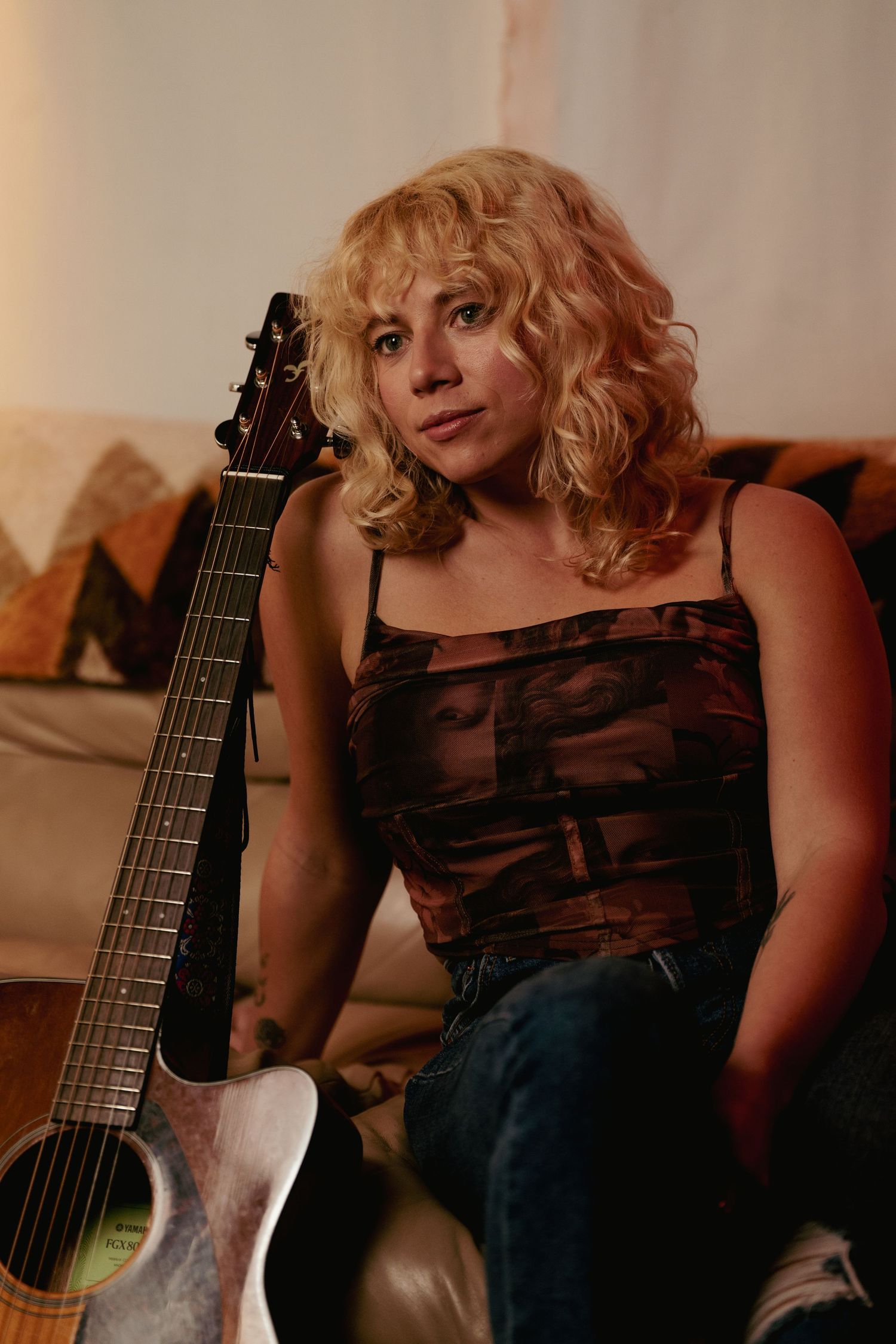 A musician relaxes with an acoustic guitar in casual attire against a warm background.
