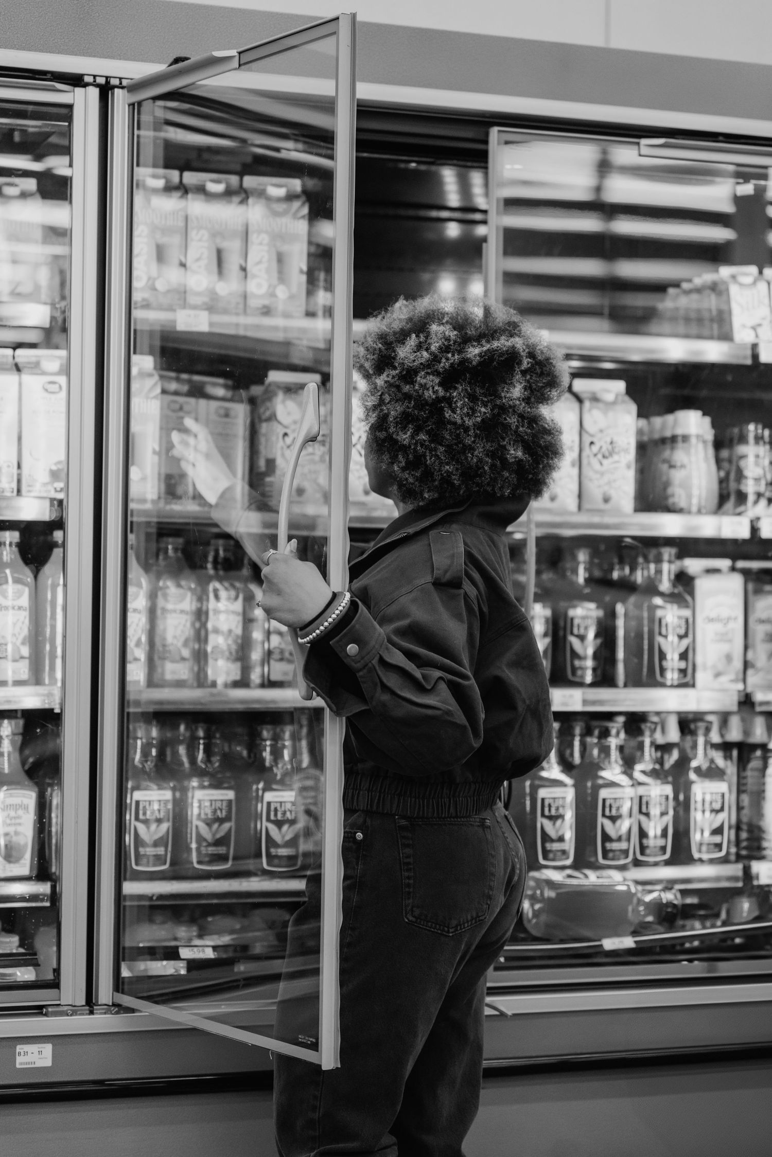 Customer selecting items from refrigerated section in black and white supermarket photo.