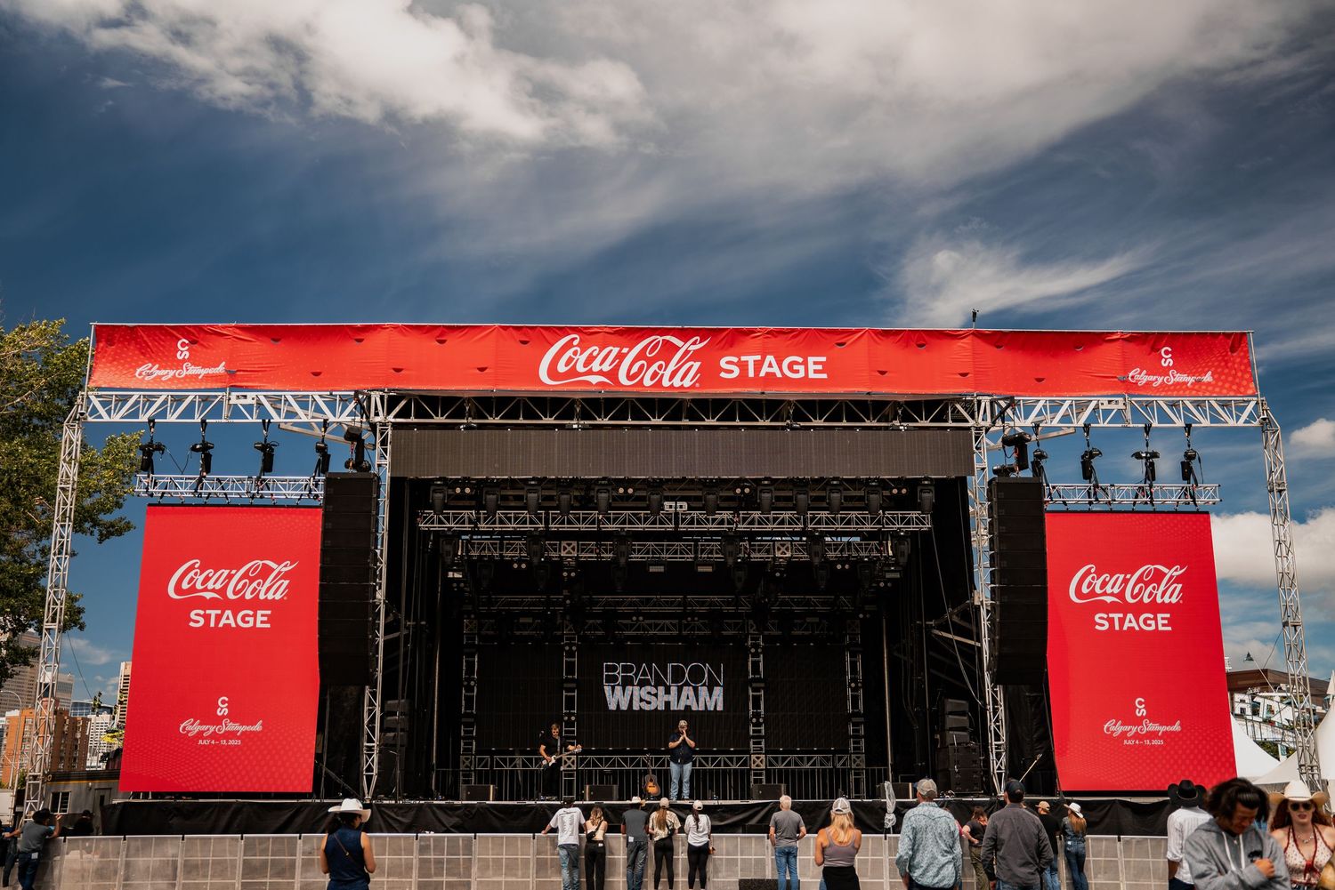 Outdoor concert venue with Coca-Cola branded signage against blue sky.