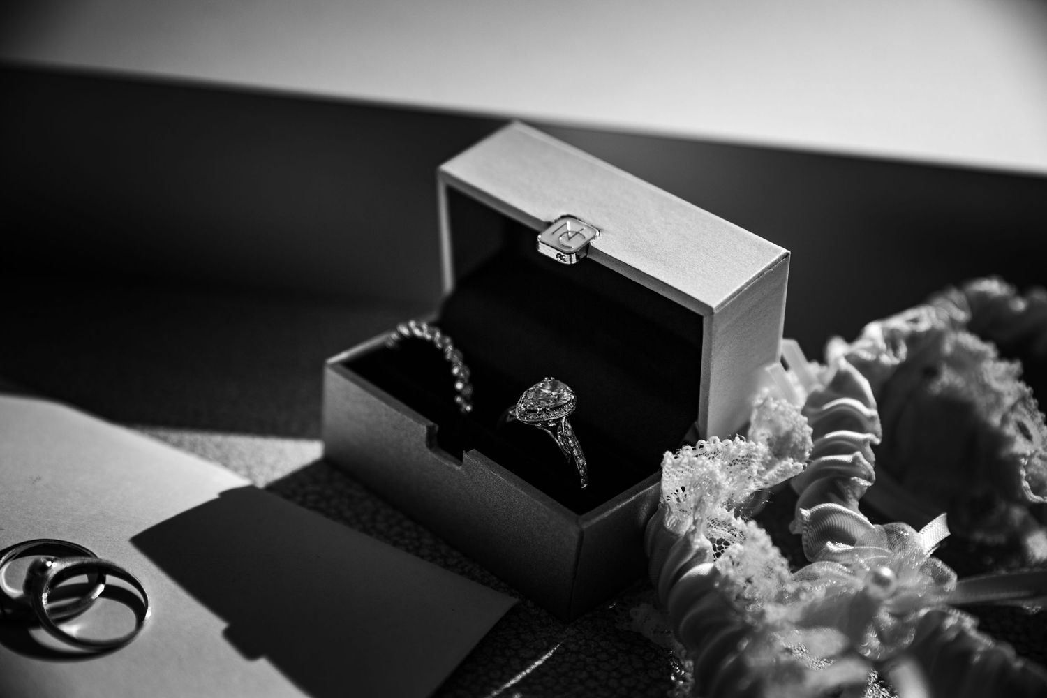 Black and white detail shot of wedding rings and jewelry boxes on dark surface.