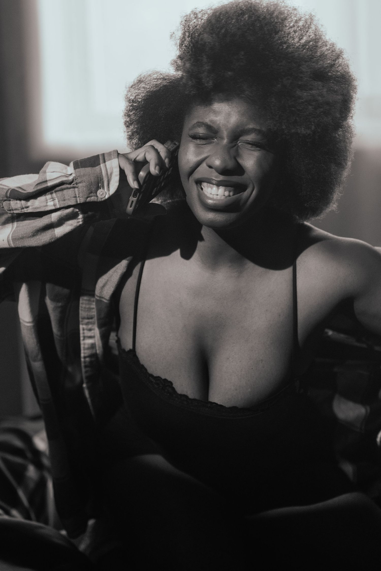 A black and white portrait of a performer with an afro hairstyle wearing a black top and smiling joyfully.