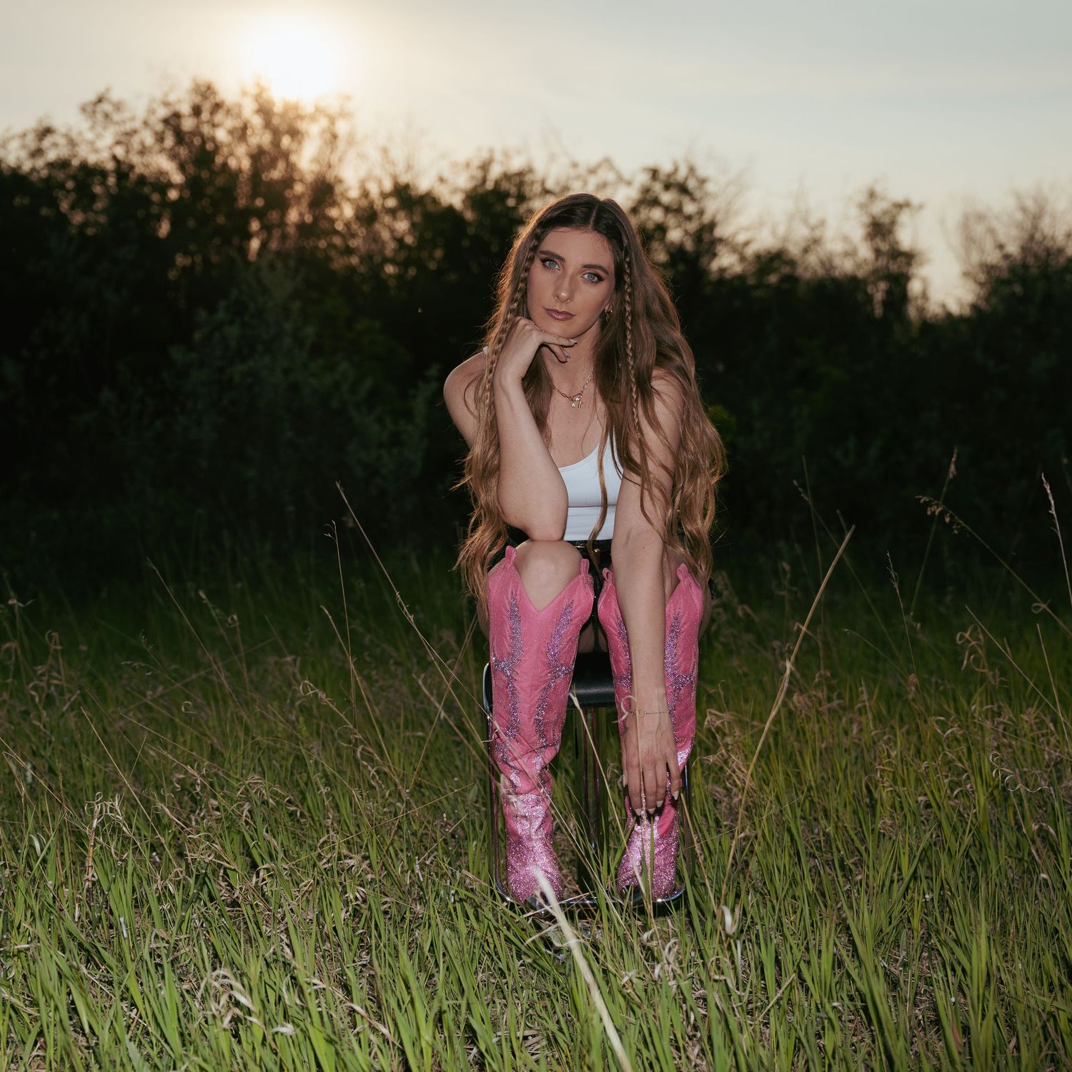 A person in pink boots sits in a grassy field at sunset.