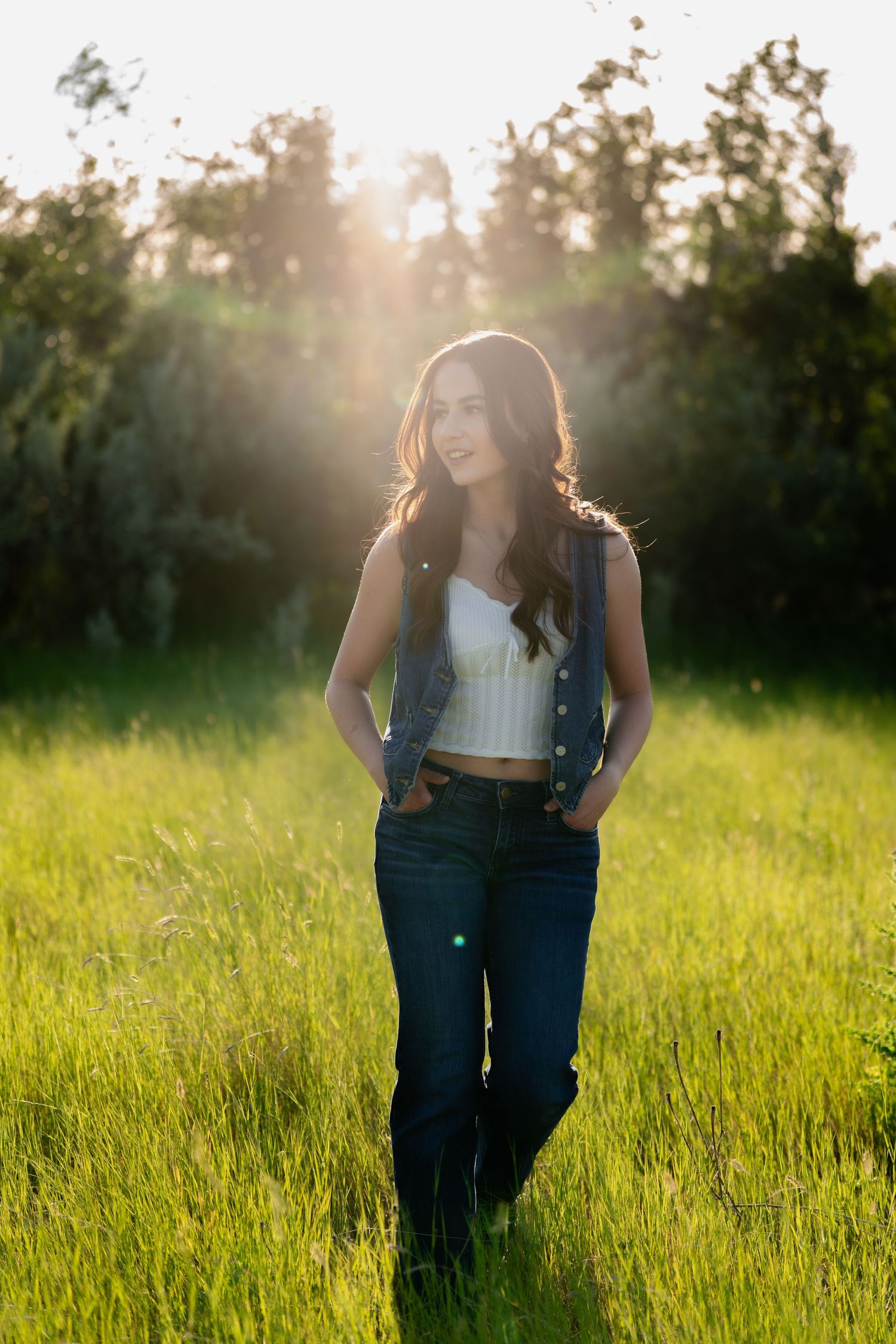 Portrait in sunlit meadow with golden hour backlighting through trees.